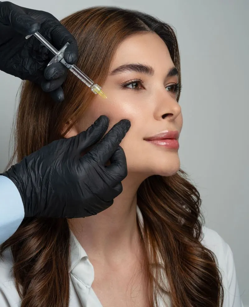 Practitioner in black gloves giving a woman an anti-wrinkle injection near the eye at a London W2 clinic