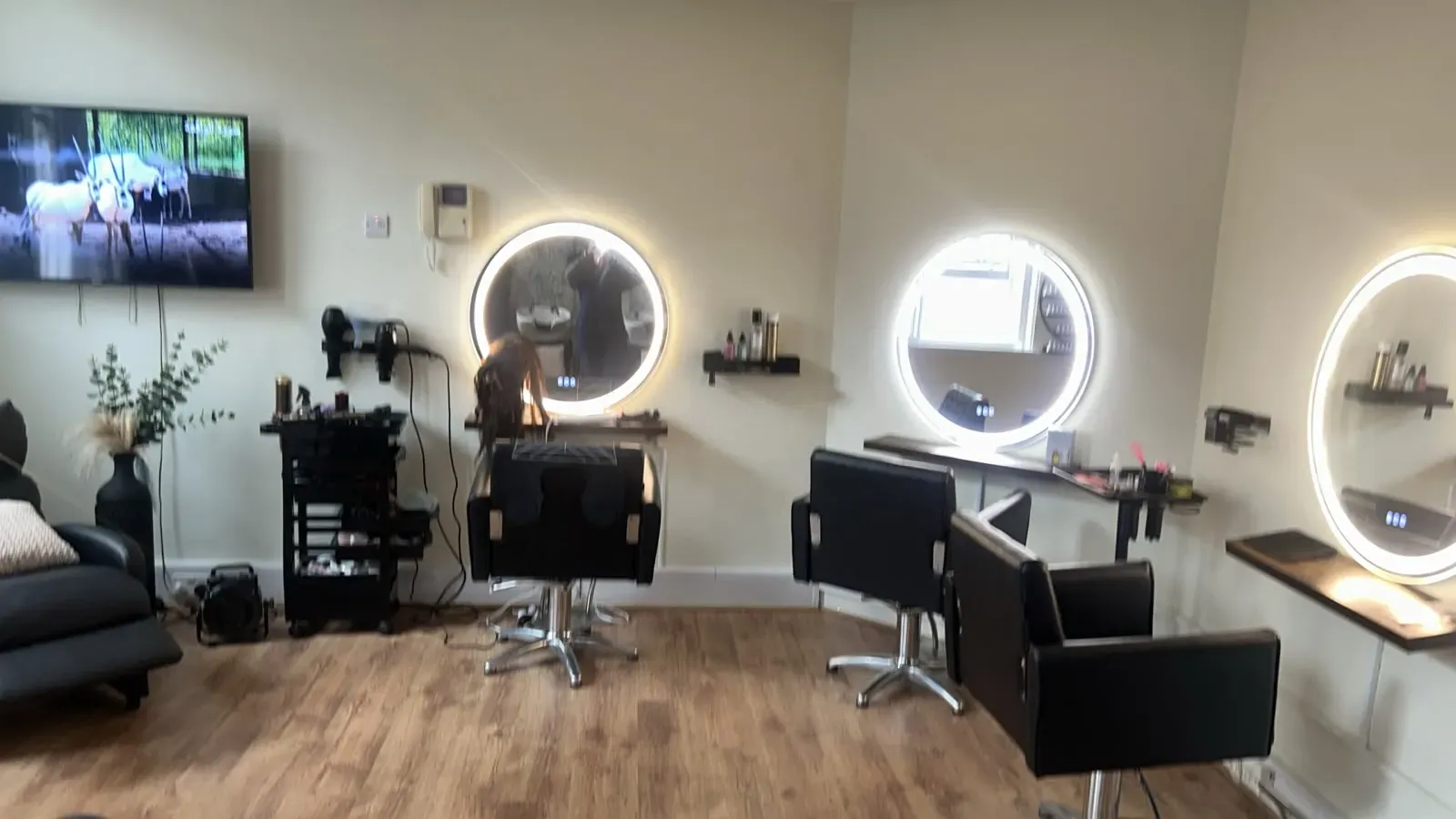 Three hair styling stations, each with a hydraulic chair and an illuminated round mirror