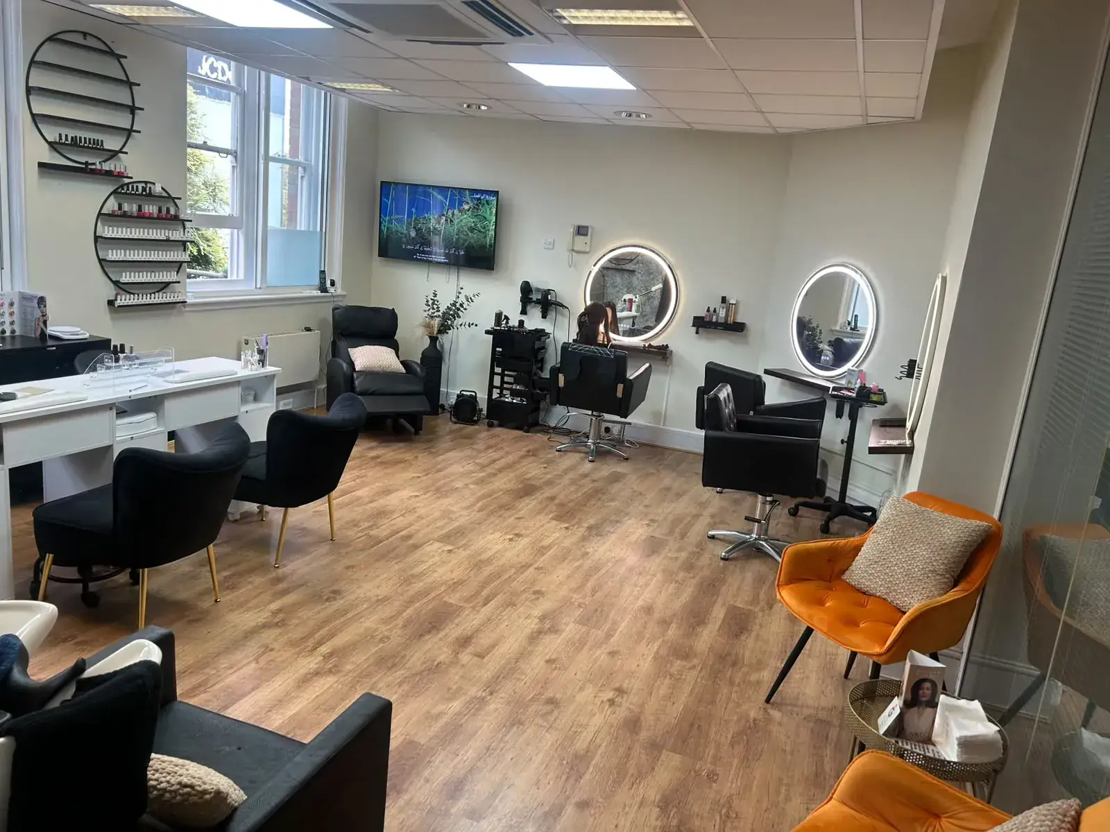 Open-plan salon floor with styling chairs, round LED mirrors, a nail desk and orange velvet armchairs