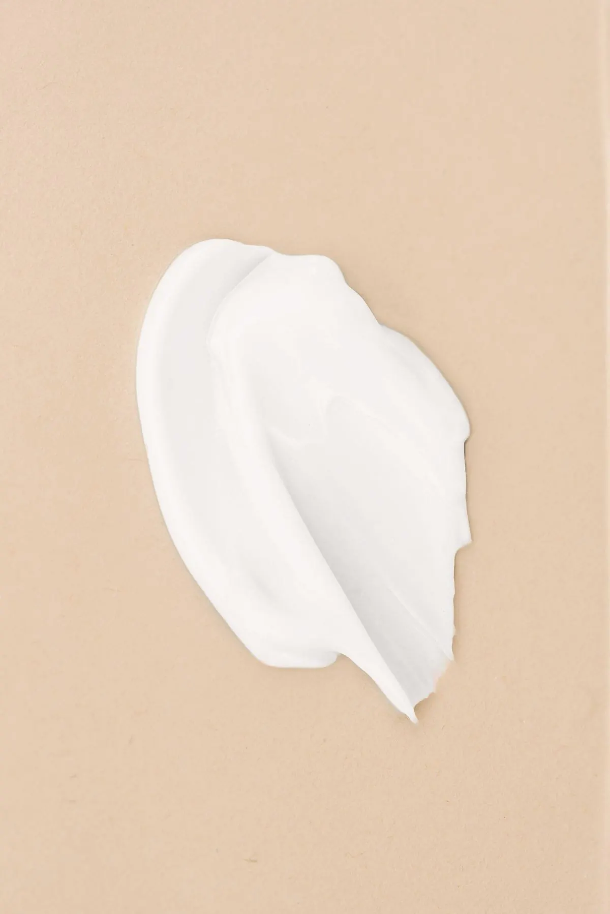 Swirl of white skincare cream on a soft peach background